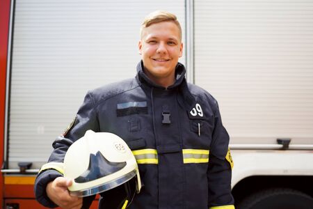 Photo of happy fireman with helmet in his hand standing near fire truck