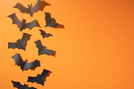 Halloween picture of black bats flying up on blank orange background.