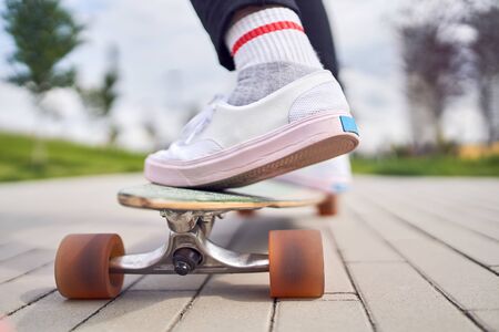 Photo of legs of girl in white shoes riding skateboard on street in cityの写真素材