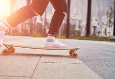 Picture of womans legs in white sneakers riding skateboard on street in city on summer day.の写真素材