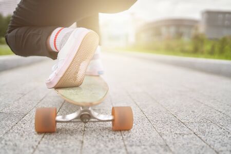 Image of woman's legs in white sneakers riding skateboard on street in city on summer day. Lensflare effectの写真素材
