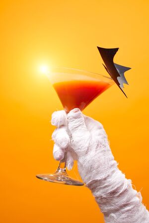 Photo of mummys hand with wine glass and black bat on empty orange background.の写真素材