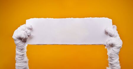 Photo of mummys hands and empty blank paper on empty orange background .の写真素材