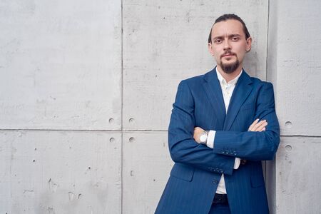 Photo of young brunet in business suit with arms crossed standing near concrete wall