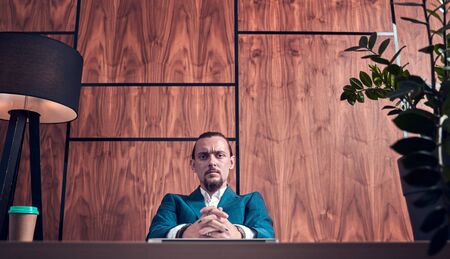 Photo of young brunet in business suit sitting at table on background of wooden wall.