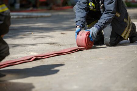 Fireman unwinding red fire hose outdoorsの写真素材