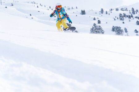 Sports woman in helmet and mask is riding on snowboard on snowy slope at winter day. Photo in full growth.の写真素材