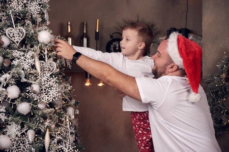 Image of father in Santas cap with his son near Christmas fir.の写真素材