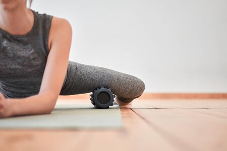 Woman stretching with massager sitting on rugの写真素材