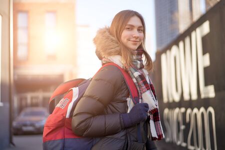 Happy woman with red backpack on walk in city on autumn day.