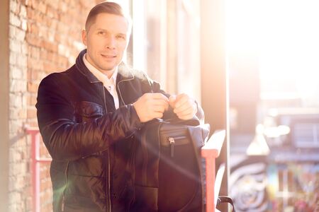 Young man with bag on walk in city against backdrop of modern buildings at day.