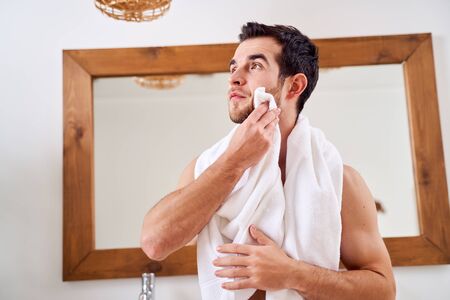 Brunet man wipes his towel while standing by mirror in bathの写真素材