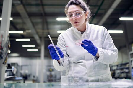 Serious young laboratory woman in glasses and petri dish in her hands conducts experiments