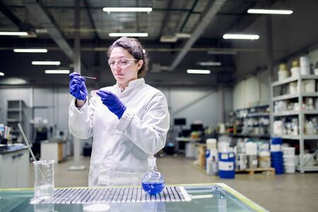 Serious lab woman in white coat with experimental glass in her hands conducts experimentsの写真素材