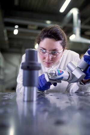 Female lab technician in blue rubber gloves with 3D printer on defocused background
