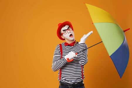 One mime with multi-colored umbrella on empty orange background