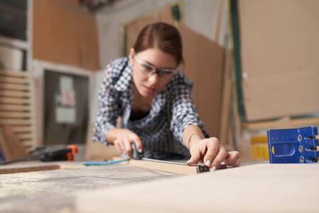 Girl woodworker with wooden board behind workbenchの写真素材