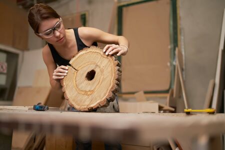 Woman carpenter in glasses with tape measure and saw cut tree in her handsの写真素材