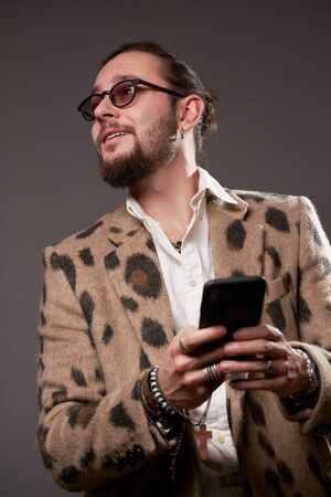 Man in sunglasses in jacket looking at side with phone in his hands on brown background