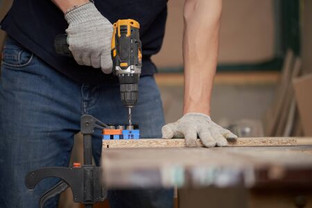Male carpenter with drill and board in workshop, close-up