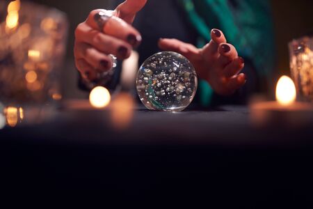 Hands of unrecognizable fortune-teller with ball of predictions in dark roomの写真素材