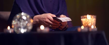 Fortuneteller woman divines on cards sitting at table with burning candles, magic ballの写真素材