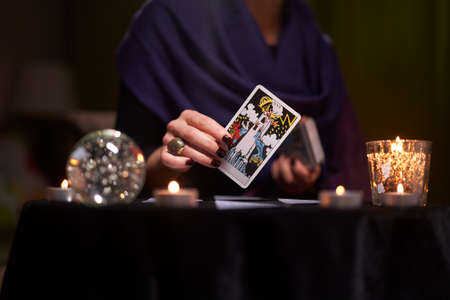 12.02.20. Moscow, Russia. Fortuneteller woman divines on cards at table with candles in dark room