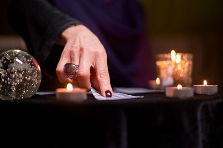 Close-up of fortune teller woman divining on cards sitting at table with burning candles, magic ballの写真素材