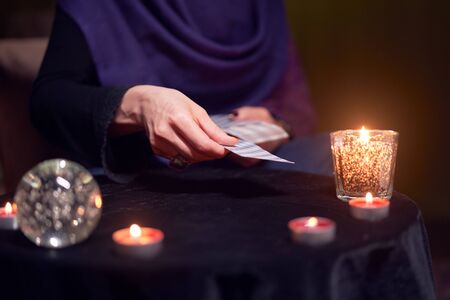 Fortuneteller woman divines on cards sitting at table with burning candlesの写真素材