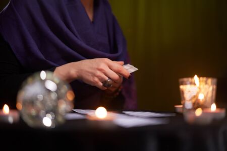 Fortune teller female in purple dress divines on cards sitting at table with candles in dark room