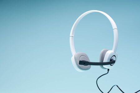 Headphones with microphone on blank blue background, place for text