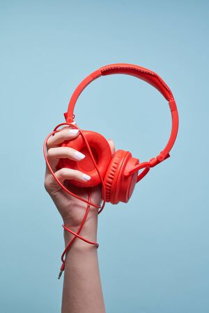 Hand holds red headphones on empty blue background, close-up