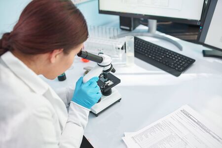 Woman laboratory assistant looking through microscope in laboratory, closeup.