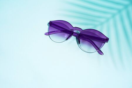 Blue sunglasses on blue background and palm leaf shadowの写真素材