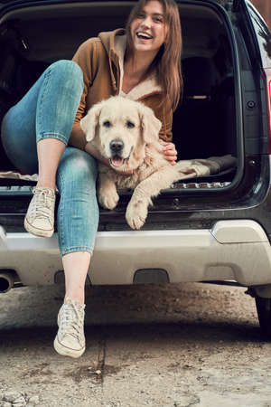 Happy woman hugs golden retriever sitting in open trunk of black carの写真素材