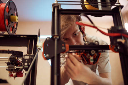 Young man fixing modern 3D printer in studio