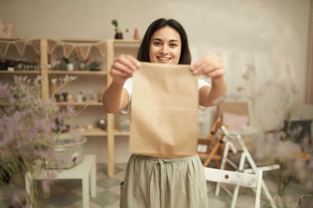 Cheerful female potter showing paper bagの写真素材