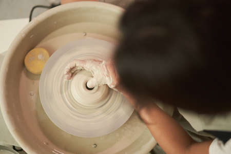 Unrecognizable craftswoman sculpting vase on wheel