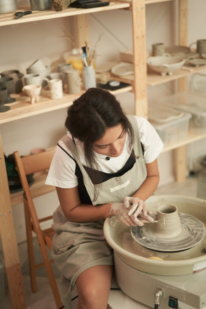 Female artisan shaping clay pot in pottery studioの写真素材