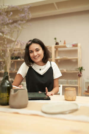 Happy craftswoman using tablet in pottery studio