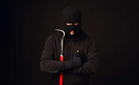Thief in black balaclava holding crowbar and black credit card. Banking and non cash thief conceptの写真素材