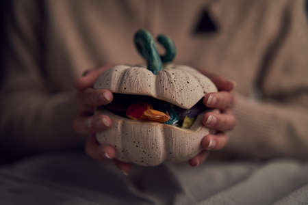 Crop woman showing pumpkin with candiesの写真素材