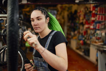 Serious woman fixing wheel of bicycle in repair shop