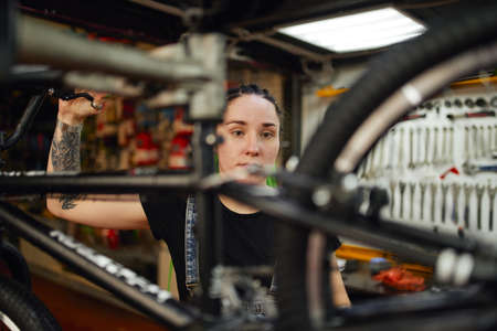 Focused woman repairing bicycle in workshopの写真素材