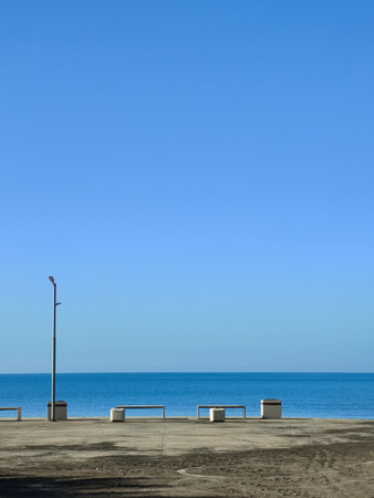 Minimalist Seafront with Benches and Lamp Post under Blue Skyの写真素材