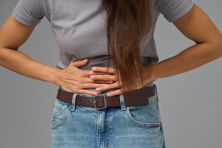 Midsection view of woman pressing lower abdomen with both hands, studio shotの写真素材
