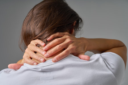 Rear view of woman holding back of neck showing pain or muscle tensionの写真素材