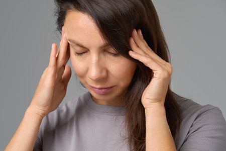 Close-up portrait of woman pressing temples with eyes closed, concept of stressの写真素材