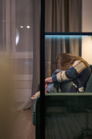 Female curled up on sofa in dimly lit roomの写真素材