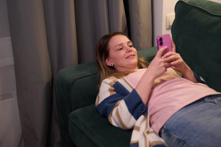 Woman lying on couch looking at smartphone indoors